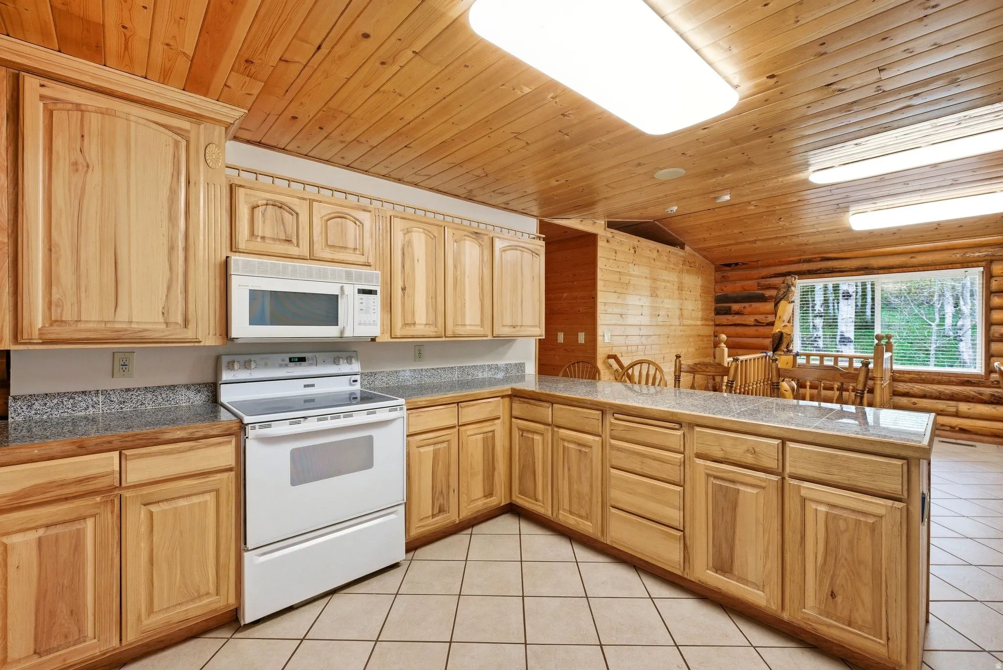 Kitchen featuring light wood cabinetry, white appliances, and a breakfast bar