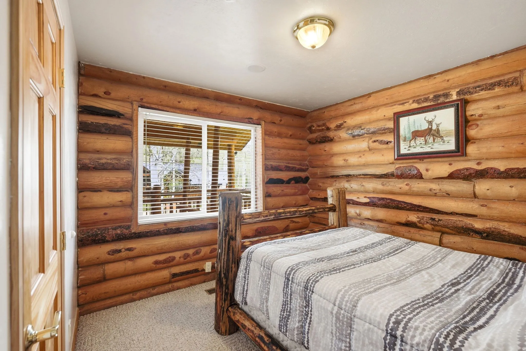 Interior room featuring log walls, carpet flooring, a natural wood door, a window with blinds, and a built-in ceiling light fixture