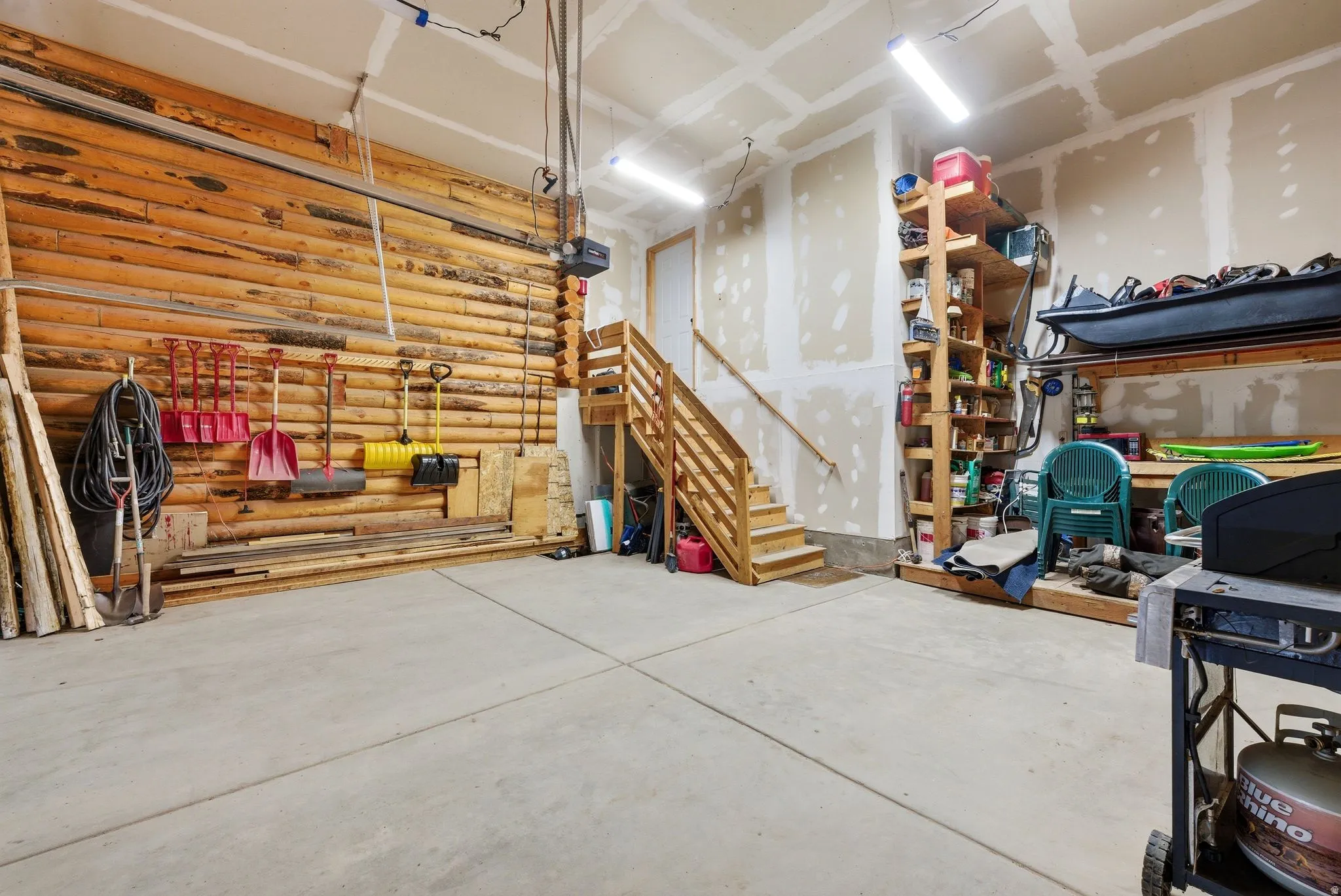 Concrete flooring garage with an exposed log wall, wood staircase, and built-in wood shelving