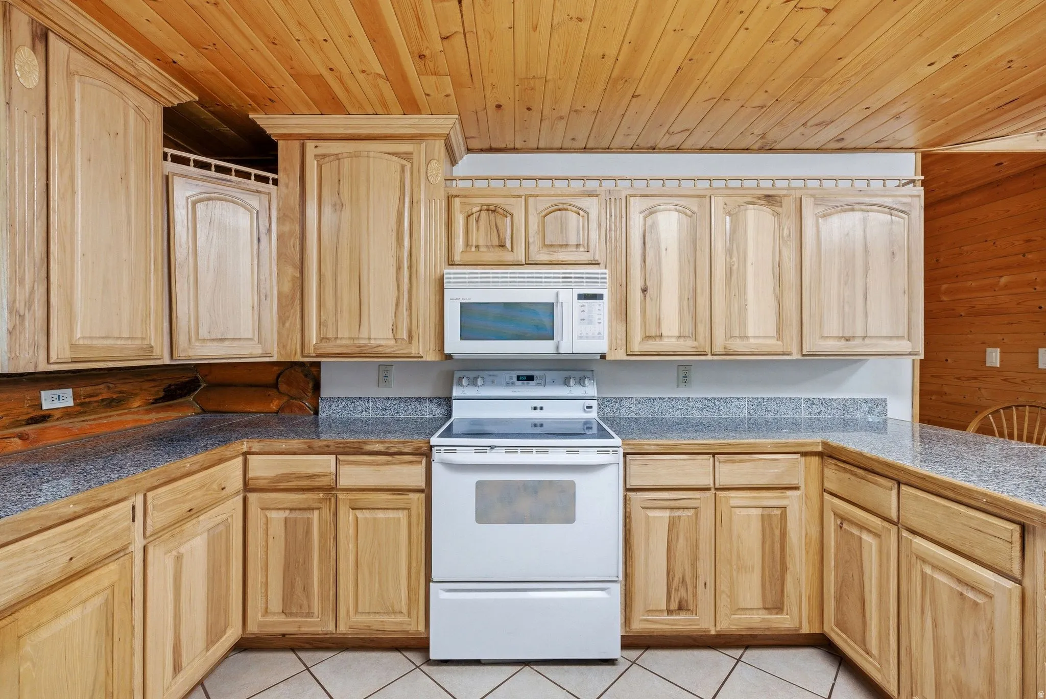 Kitchen featuring wood-finish cabinetry, granite-style countertops, white appliances, wood-paneled ceiling, and tile flooring