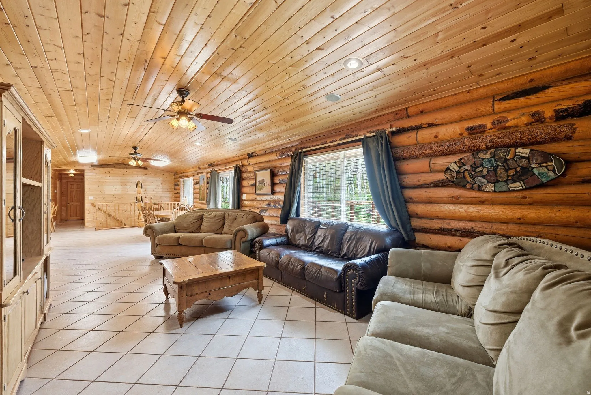 Spacious living area featuring log walls, wood-paneled ceilings, and ceramic tile flooring