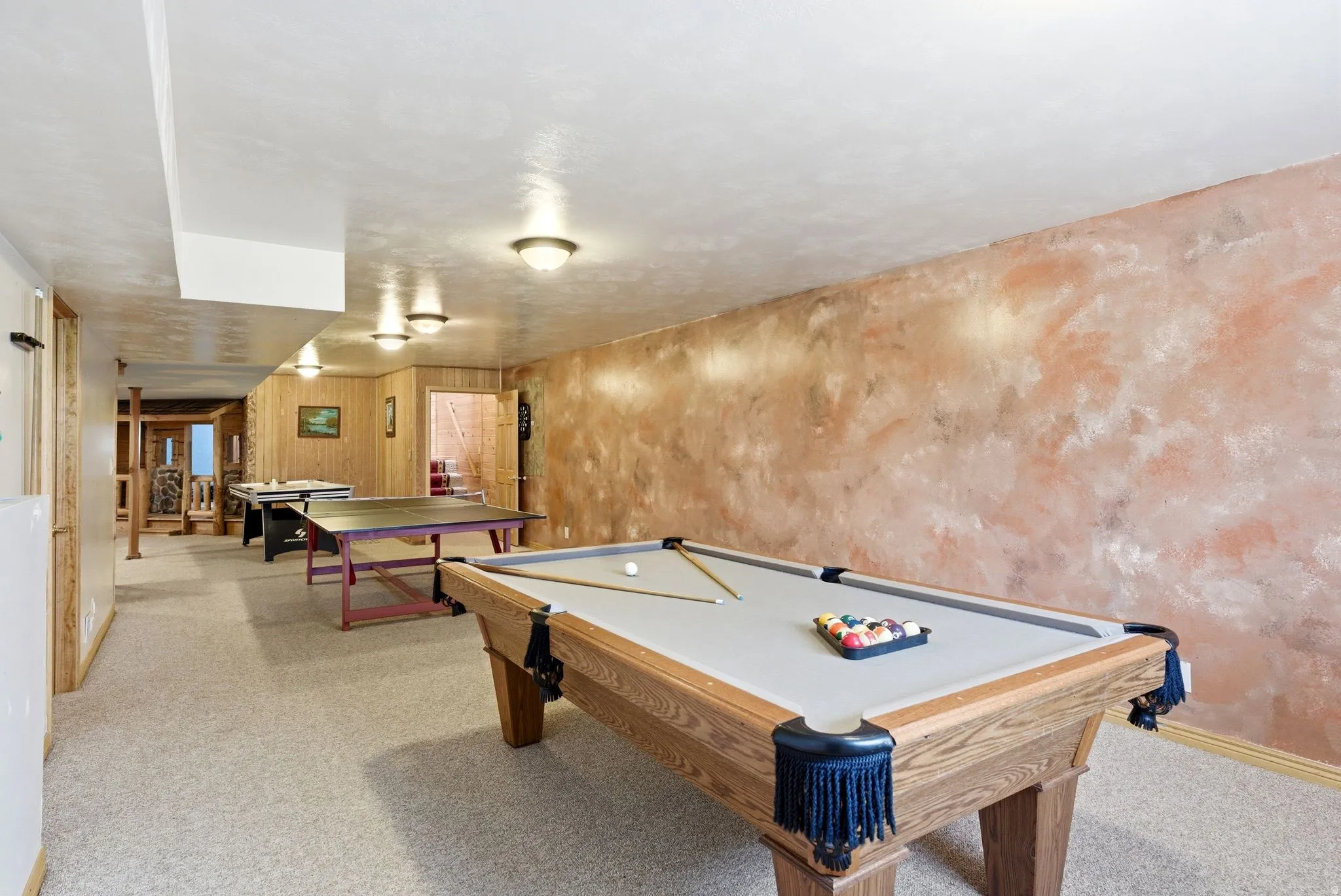 Expansive recreation room featuring a billiard table, carpet flooring, wall sconce lighting, wood paneling, and a unique textured wall finish