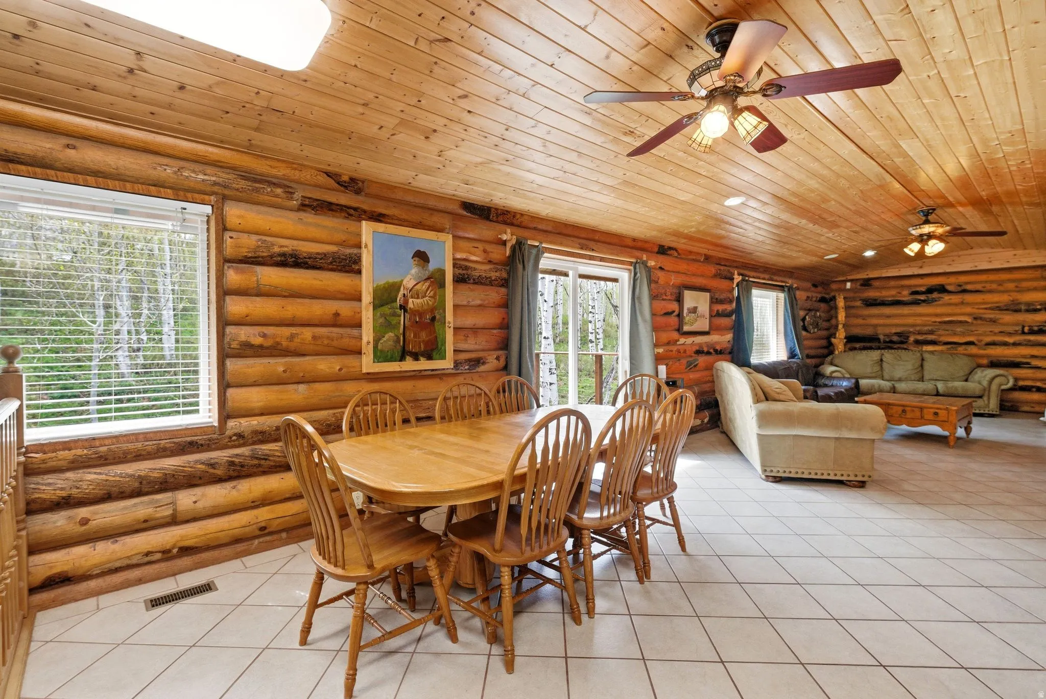 Open-concept living area featuring log walls, wood-paneled ceilings, and light-toned tile flooring