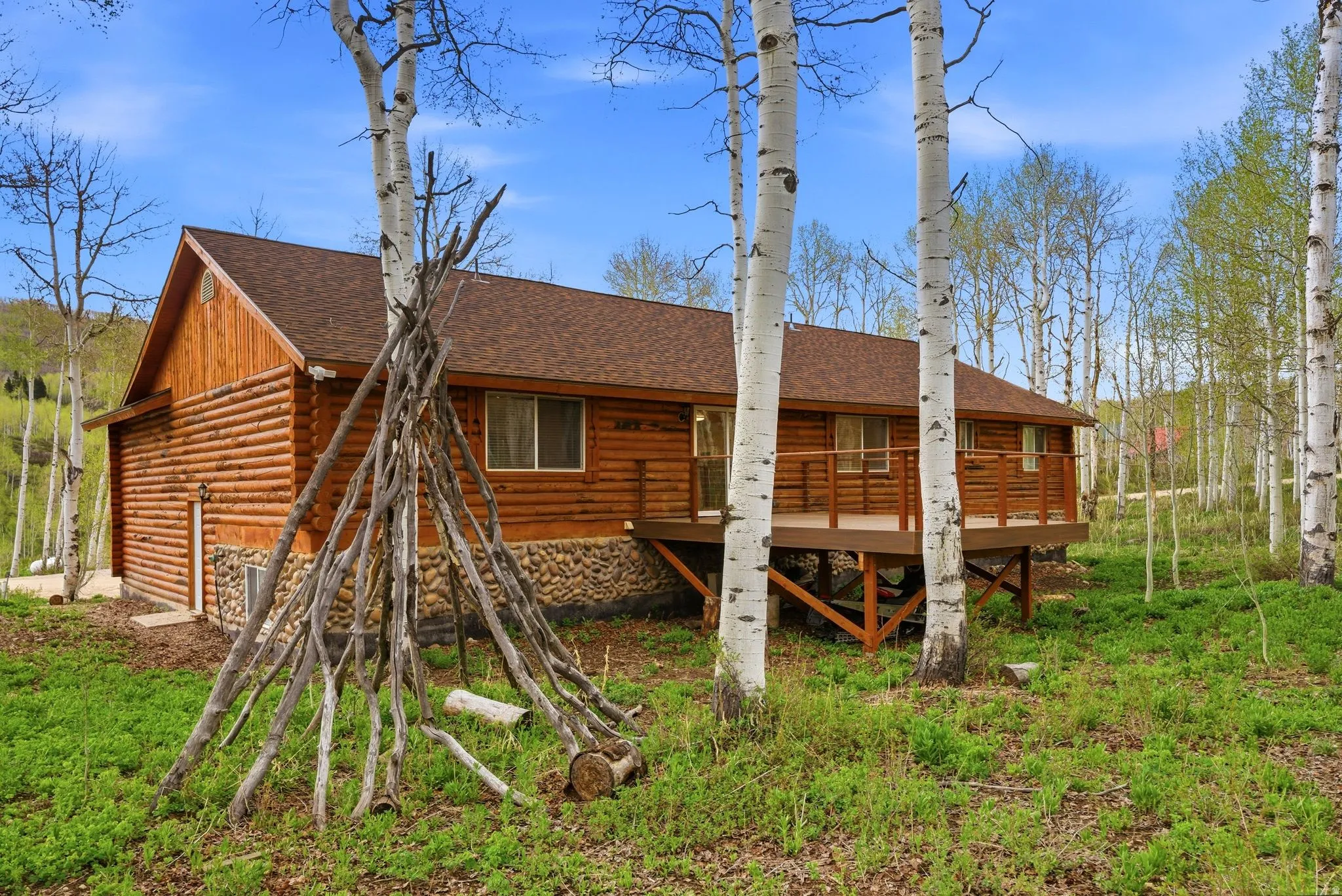 Wood-sided cabin featuring a brown shingle roof and a raised wooden deck with railings