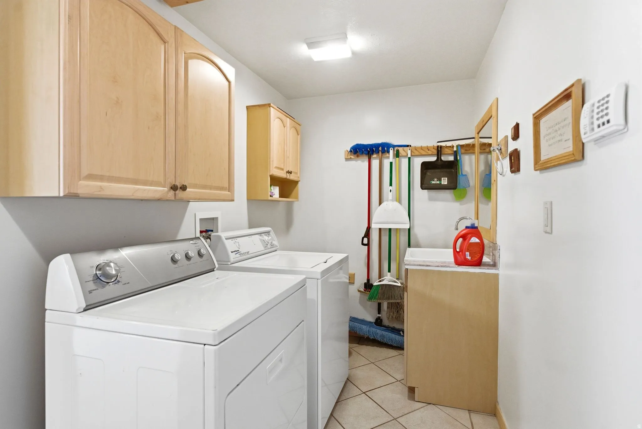 Bright laundry area featuring light wood cabinetry, a utility sink with a vanity, and tile flooring