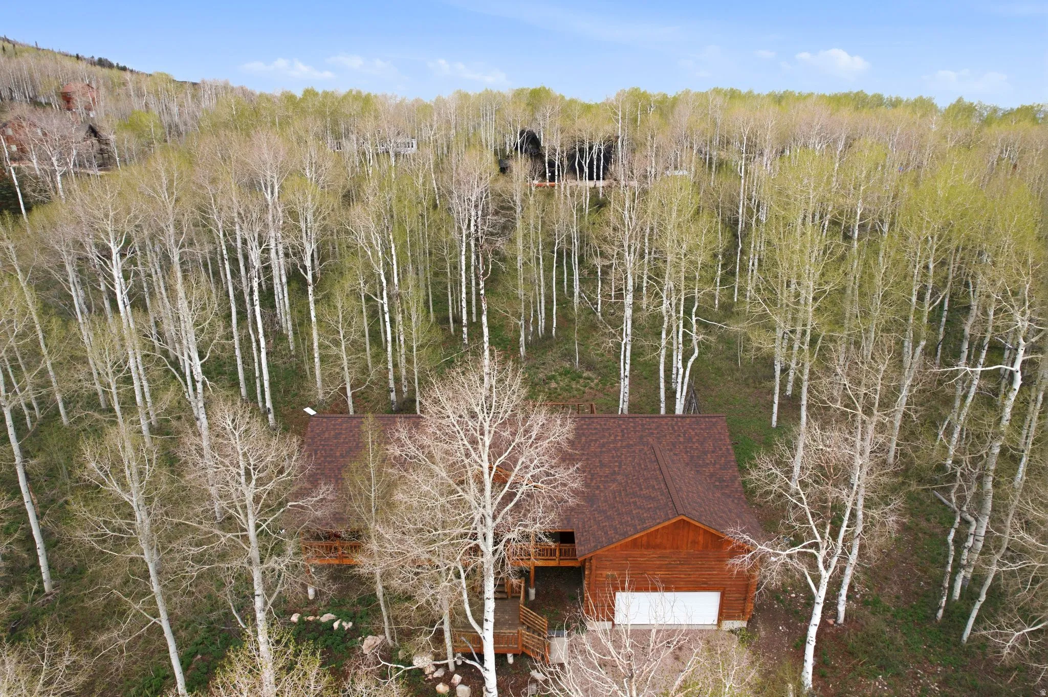 Wood-sided residence with a brown shingle roof, surrounded by mature trees