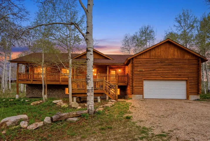 Log cabin exterior featuring a covered porch, wood railing, stone foundation elements, and an attached two-car garage