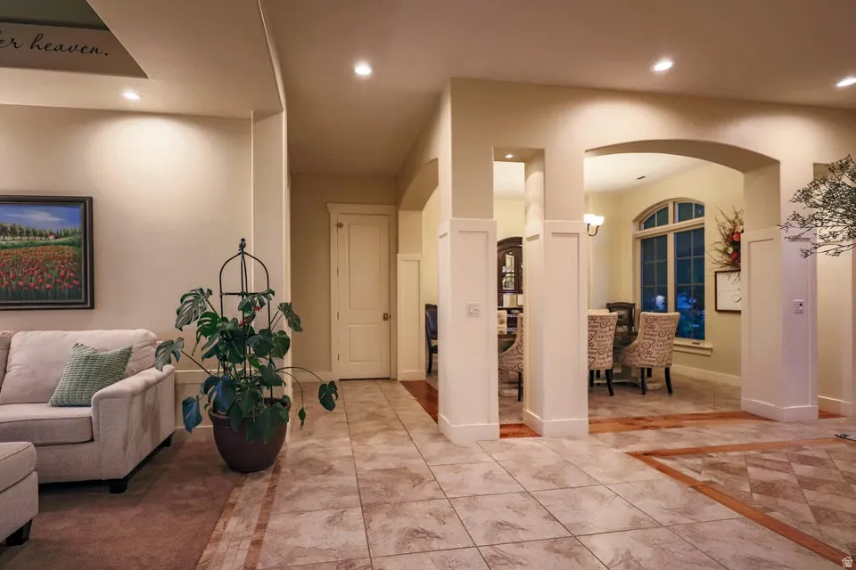 Expansive tiled flooring with accent border, arched doorway to dining area, recessed lighting, and white paneled walls