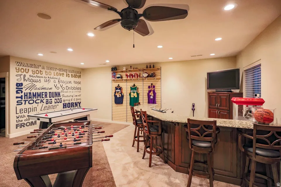 Entertainment space featuring a built-in bar with stone-finish countertop, recessed lighting, ceiling fan, and carpet flooring