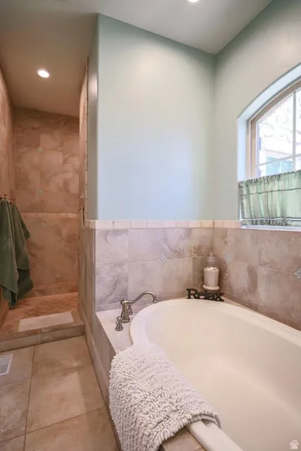 Built-in soaking tub with deck-mounted faucet, complemented by a tiled surround and an arched window