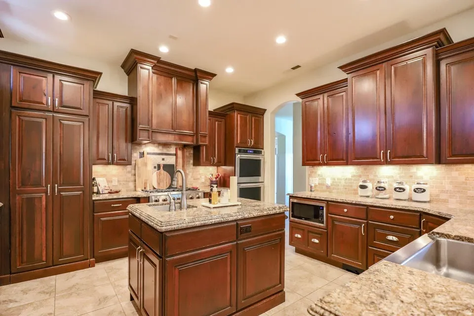 Kitchen featuring wood cabinetry, granite countertops, tile flooring, and stainless steel appliances including a built-in microwave and double wall ovens