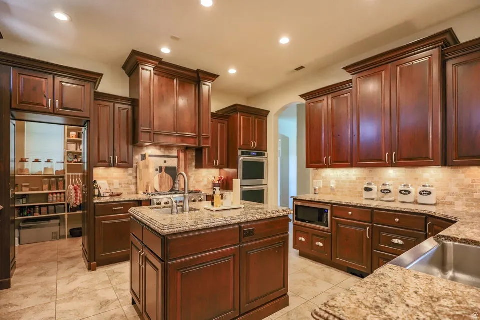 Kitchen featuring rich wood cabinetry, granite countertops, stainless steel appliances, a tiled backsplash, and recessed lighting