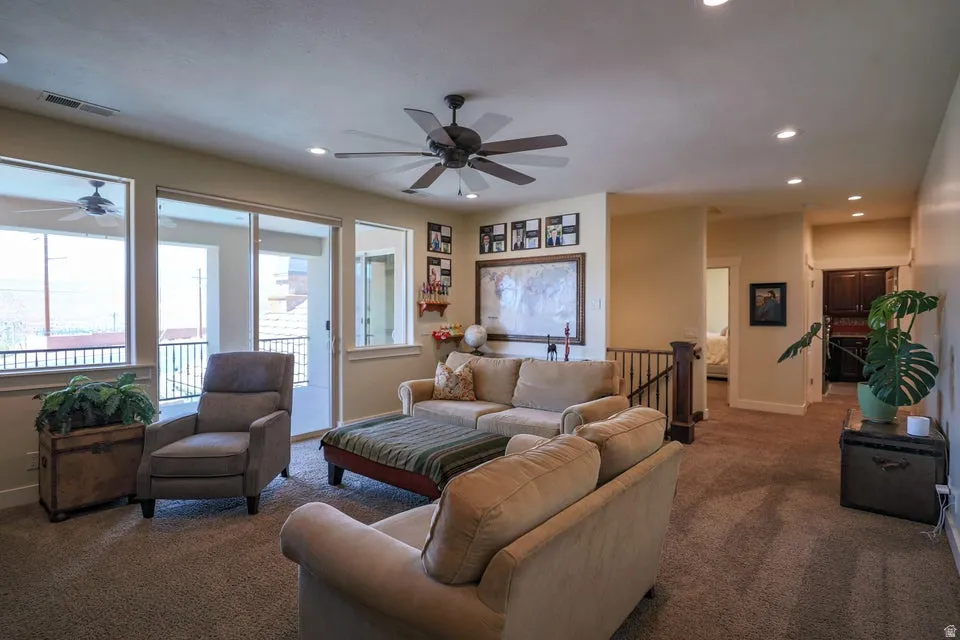 Carpeted living area featuring a ceiling fan, recessed lighting, and a sliding glass door opening to an outdoor balcony with a black railing