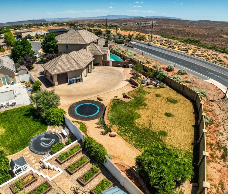 Expansive rear yard featuring multiple terraced levels, a built-in swimming pool, a dedicated garden area with raised beds, and a large paved driveway leading to a three-car garage