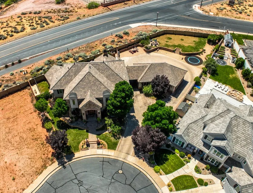 Spacious property featuring a large residence with a multi-gabled roof, extensive hardscaping, mature landscaping, and an expansive lawn area