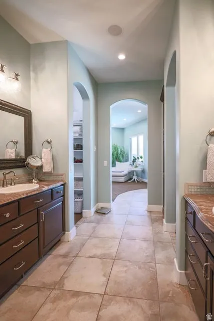Tiled flooring leads through an arched entryway, flanked by dark wood vanities with integrated sinks and stone-finish countertops