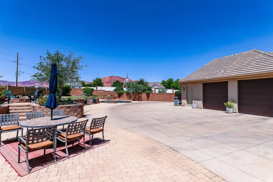 Expansive outdoor living area featuring a paved patio, multi-level landscaping with retaining walls, and a large concrete driveway leading to a two-car garage