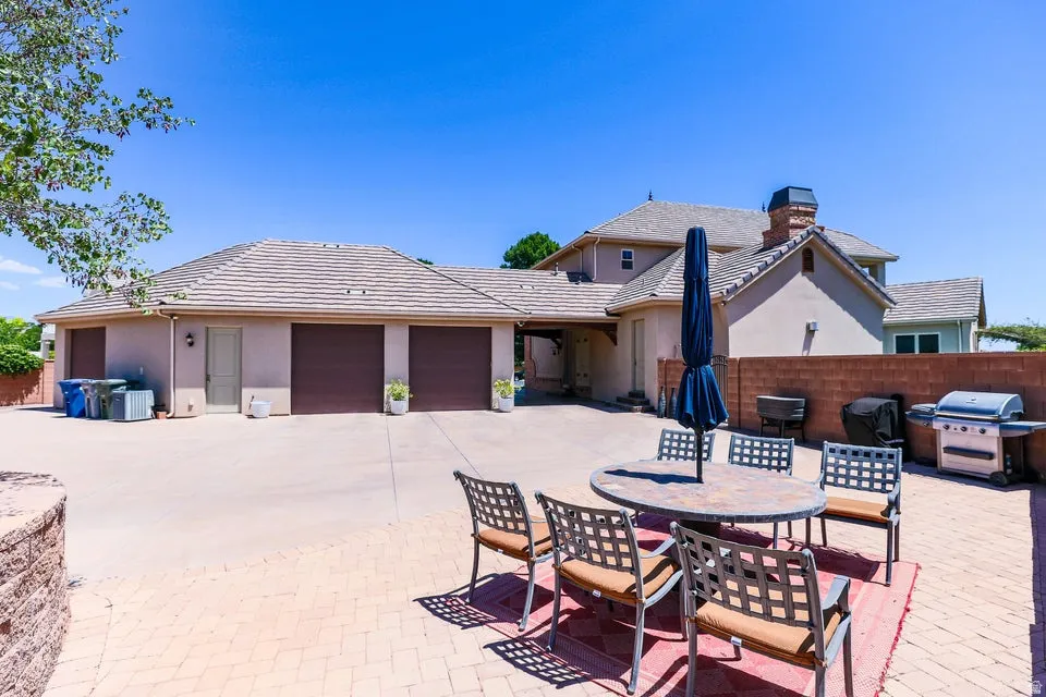 Spacious paved patio area featuring a stone tile-top table with seating, a brick retaining wall, and a large multi-car garage with individual doors