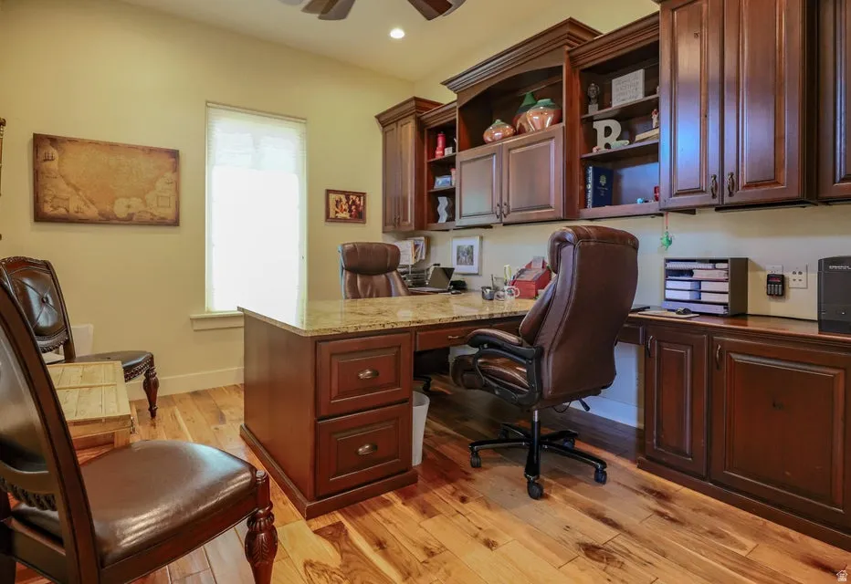 Dedicated workspace featuring extensive custom cabinetry, wood-finish flooring, a built-in desk with a stone countertop, and recessed lighting