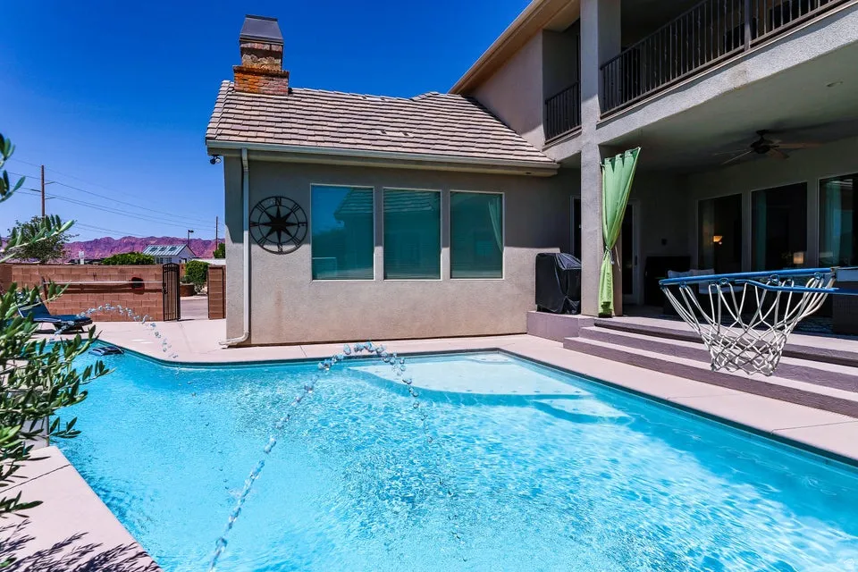 Exterior stucco dwelling featuring a rectangular swimming pool with water features, a tiered patio with integrated steps, a covered outdoor living area, and a second-story balcony