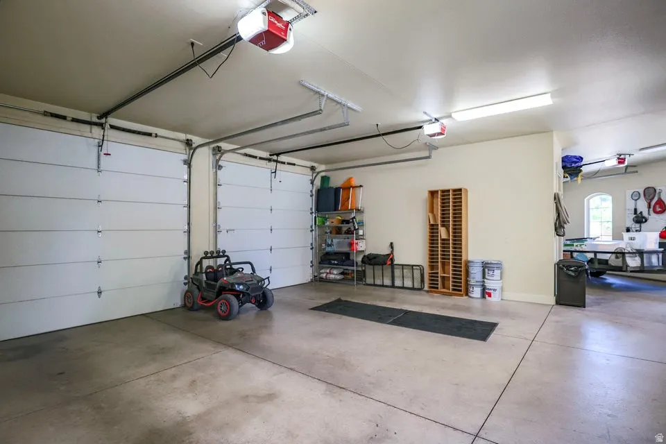 Spacious garage featuring two automatic garage doors, polished concrete flooring, overhead fluorescent lighting, and a partially visible arched window
