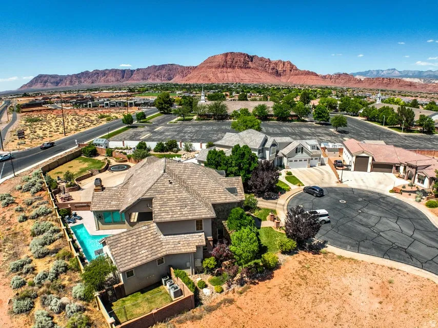 Expansive aerial capturing a property with a distinct shingle roof, a private swimming pool, and a paved patio area