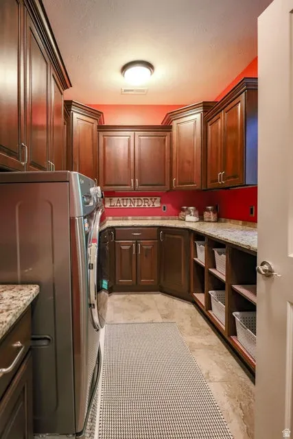 Laundry room featuring extensive dark wood cabinetry, granite countertops, built-in shelving, tile flooring, and a flush mount ceiling light fixture