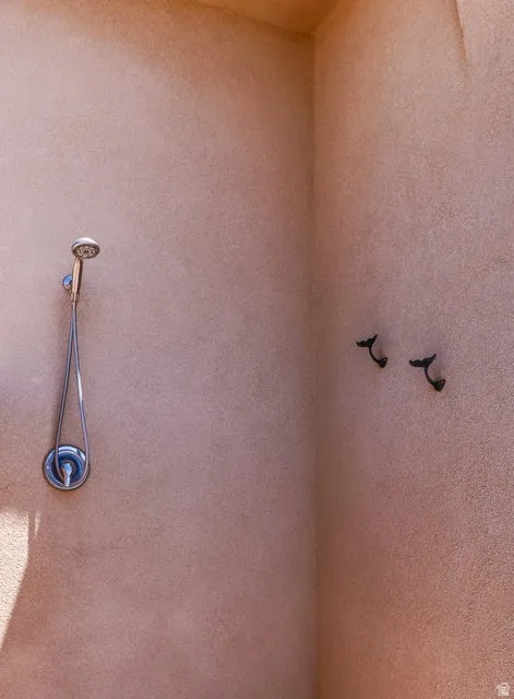 Outdoor shower with a brushed nickel showerhead and two dark-toned wall hooks, set against a stucco wall