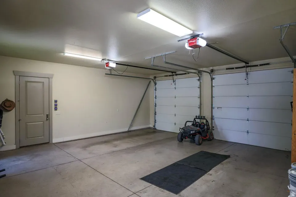 Two-car garage featuring automatic openers, fluorescent lighting, and a side access door with trim detail