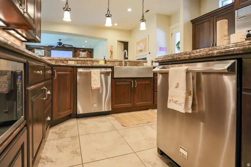 Kitchen featuring dark wood cabinetry, granite countertops, stainless steel appliances, ceramic tile flooring, and a farmhouse sink