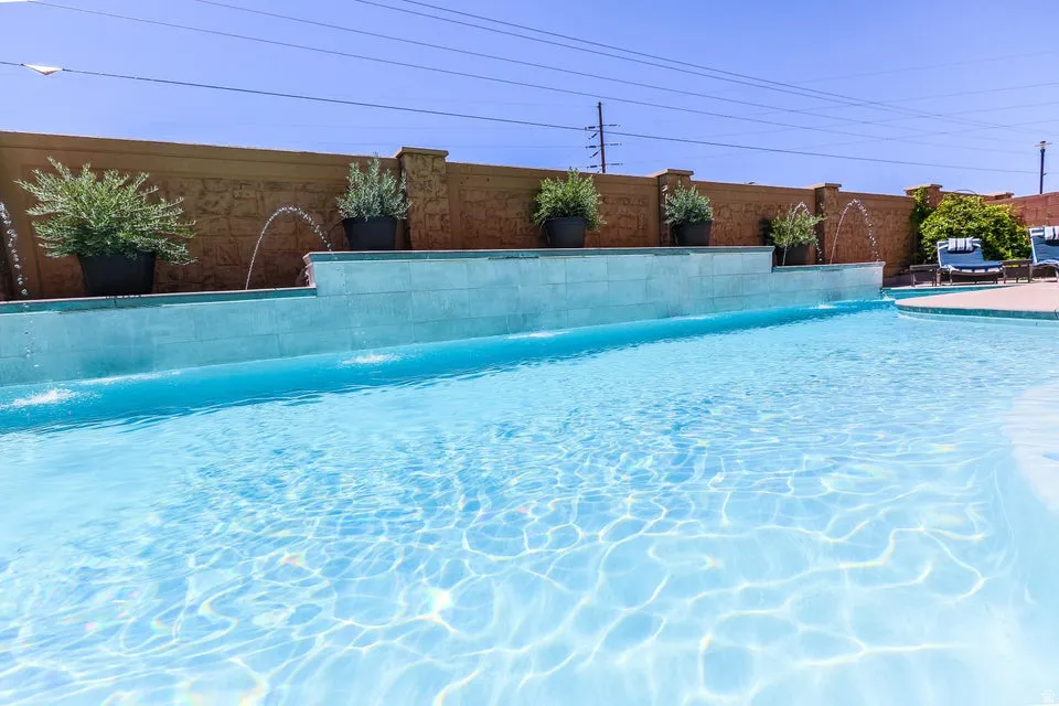 Resort-style pool with a tiered water feature, light-toned tile detailing, and a decorative privacy wall