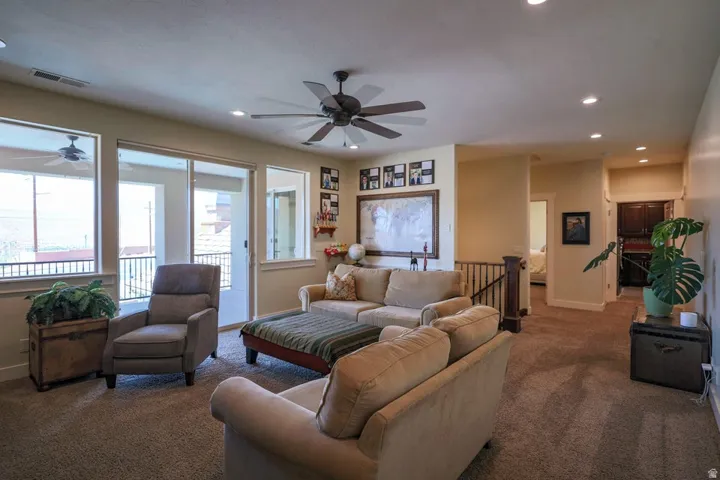 Carpeted living area featuring a ceiling fan, recessed lighting, and a sliding glass door opening to an outdoor balcony with a black railing