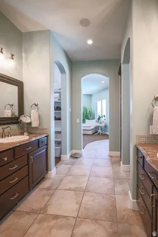 Tiled flooring leads through an arched entryway, flanked by dark wood vanities with integrated sinks and stone-finish countertops