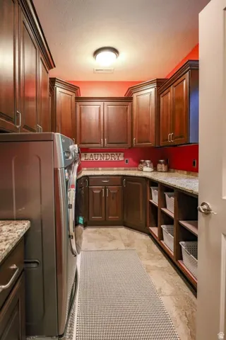 Laundry room featuring extensive dark wood cabinetry, granite countertops, built-in shelving, tile flooring, and a flush mount ceiling light fixture