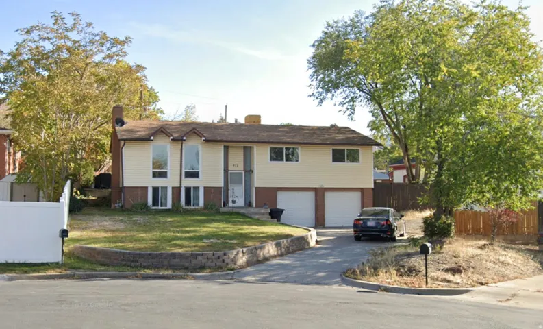 Split-level residence featuring a light-colored siding exterior, a prominent chimney, and a dual garage with white doors