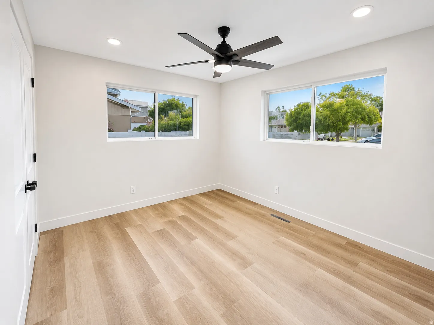 Spacious room featuring wood-finish flooring, crisp white walls, and a contemporary ceiling fan with integrated lighting