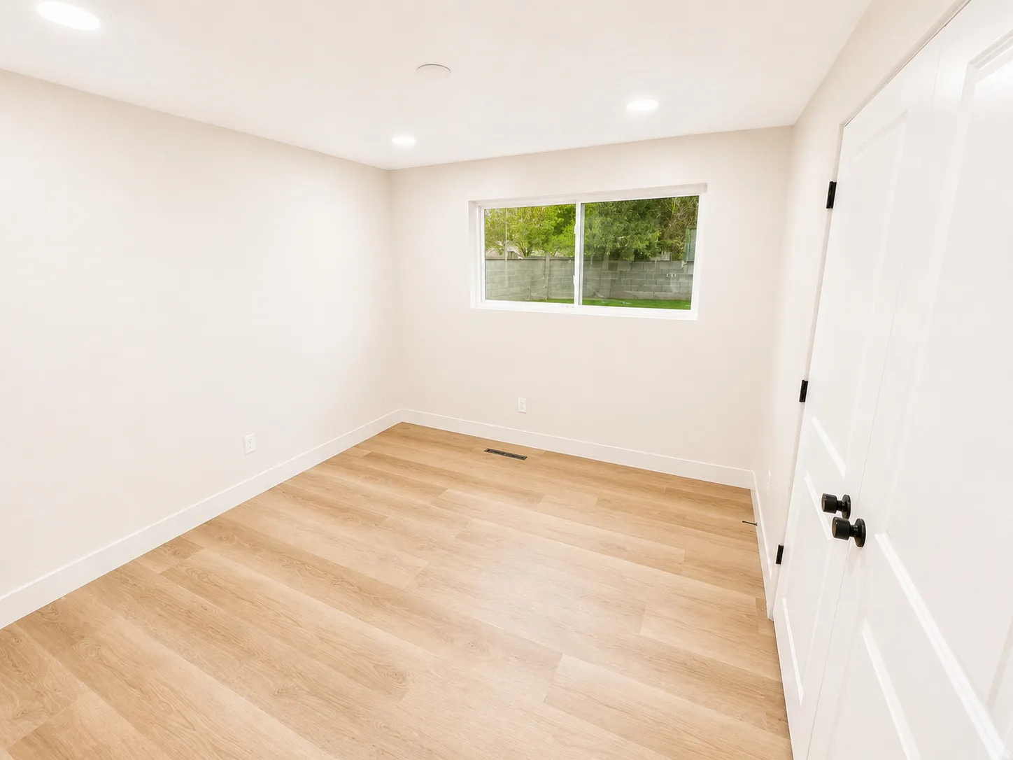 Bright interior space featuring light wood-finish flooring, recessed lighting, and a white interior door with black hardware