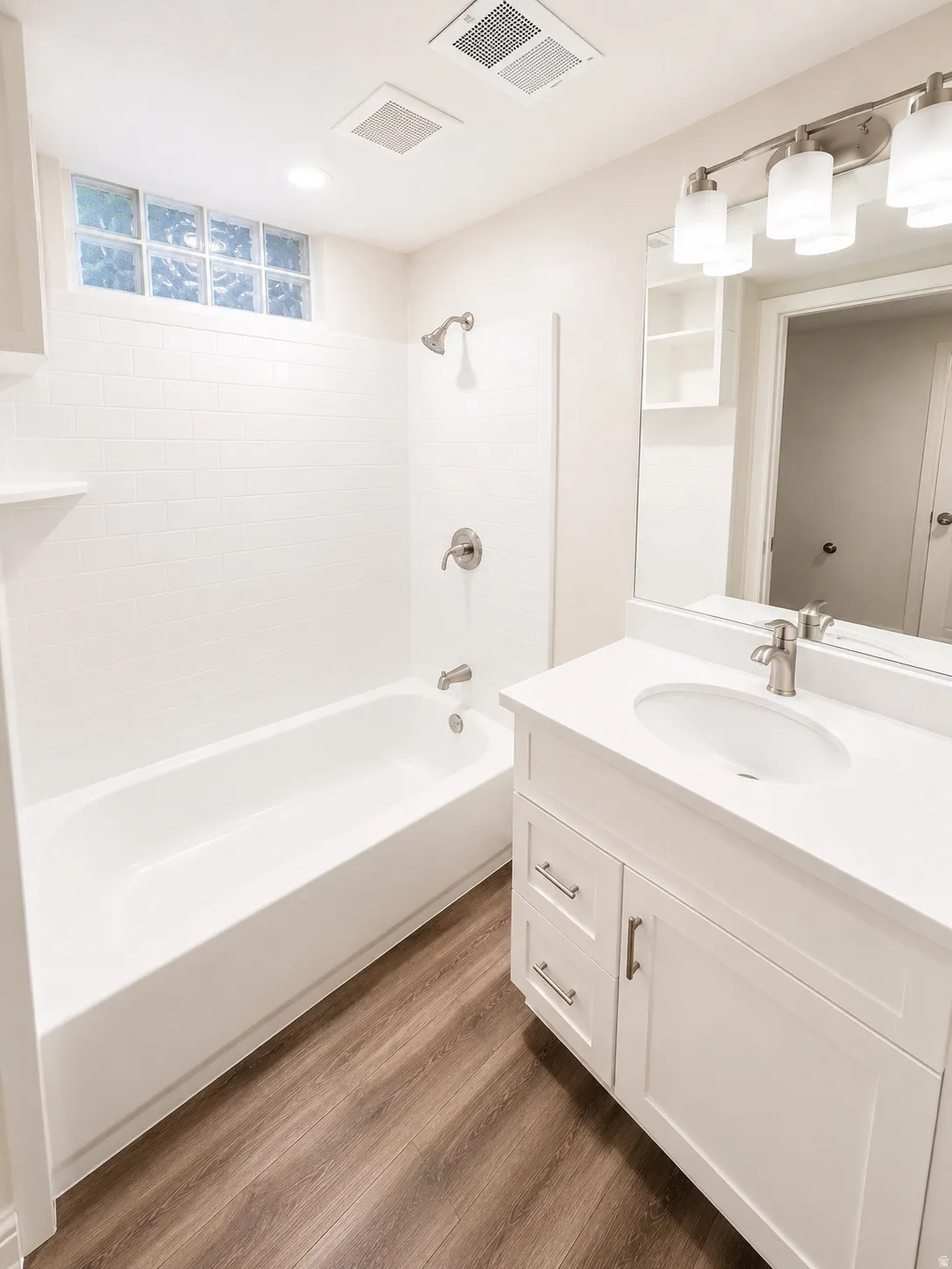 Full bathroom featuring a white vanity with an undermount sink, a white bathtub with subway tile surround, and wood-finish flooring