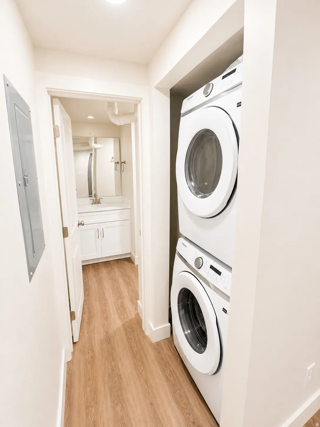 Stacked laundry appliances in a dedicated alcove, featuring light wood-finish flooring, white baseboards, and bright overhead lighting
