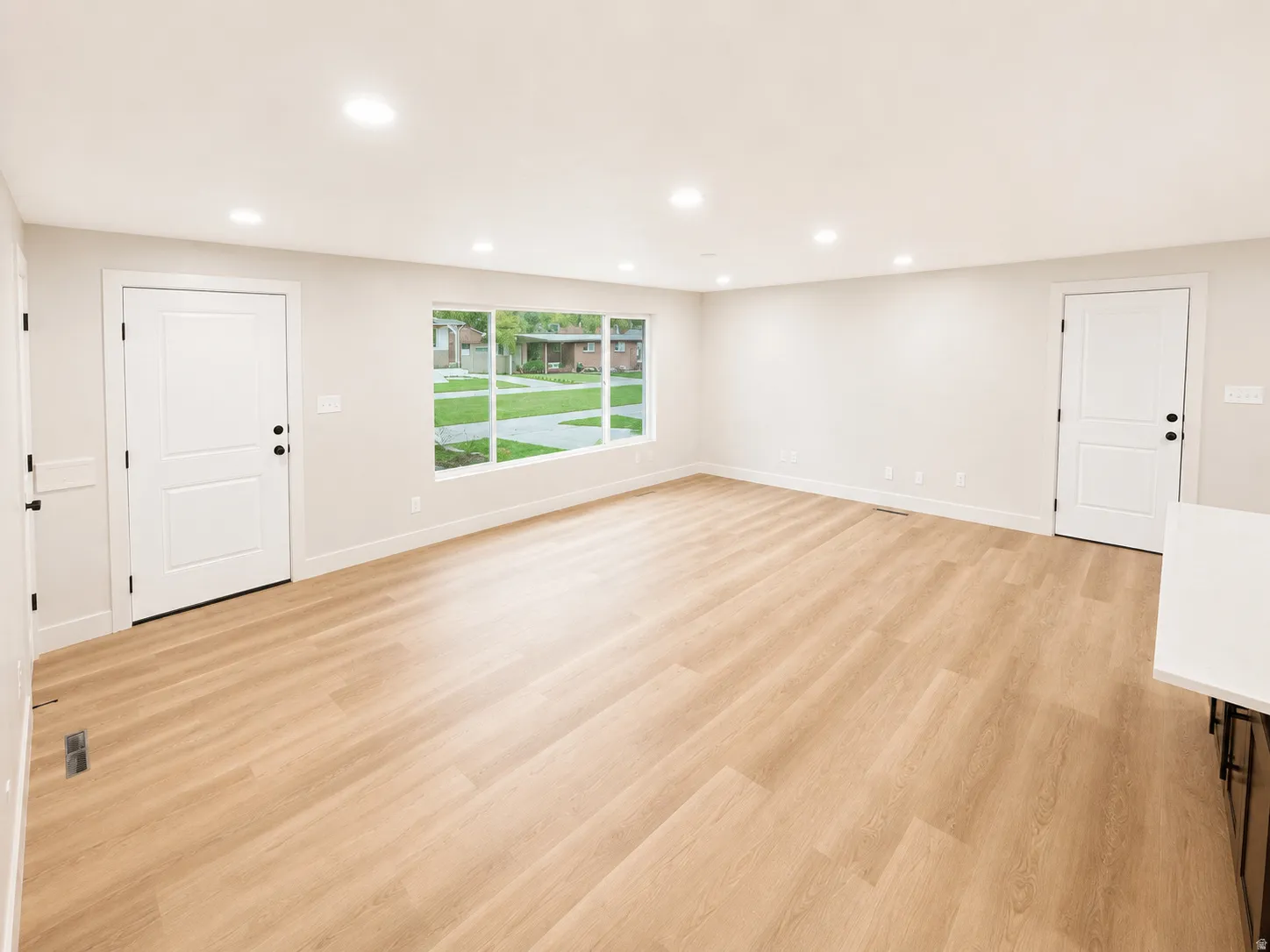 Spacious living area featuring light wood-finish flooring, recessed lighting, and a large multi-pane window