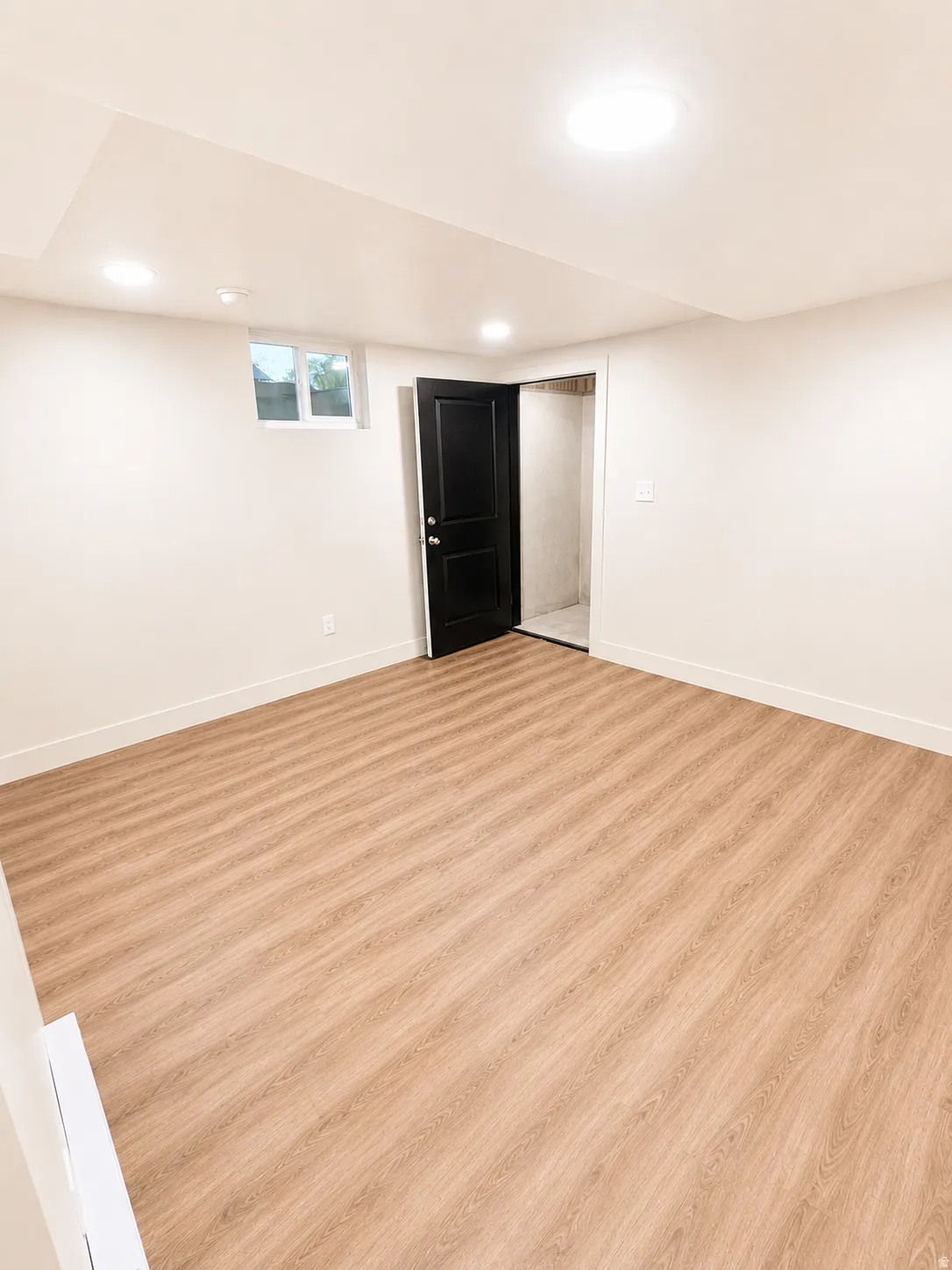 Spacious room featuring wood-finish flooring, white baseboards, and light-toned walls