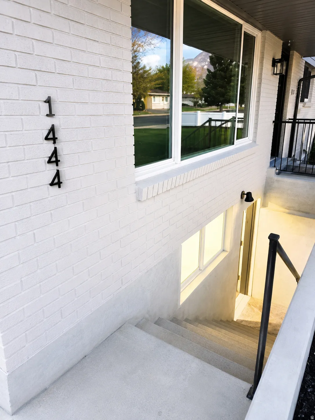 White brick exterior with modern house numbers, large picture window, and exterior wall sconces