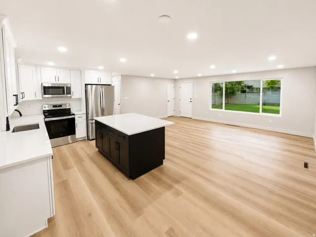 Open-concept living space featuring a modern kitchen with white cabinetry, stainless steel appliances, and a dark-toned island with a white countertop