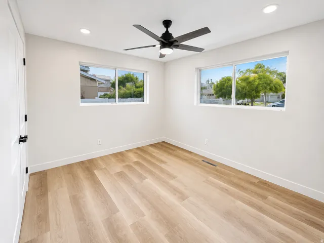 Spacious room featuring wood-finish flooring, crisp white walls, and a contemporary ceiling fan with integrated lighting