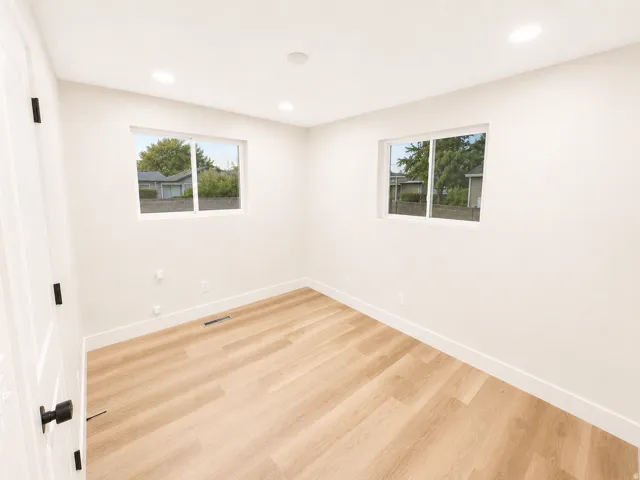 Light-filled room featuring two windows, recessed lighting, wood-finish flooring, white baseboards, and a white interior door with matte black hardware