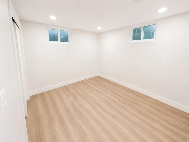 Bright room featuring light wood-finish flooring, white walls, two recessed ceiling lights, and two high-set windows