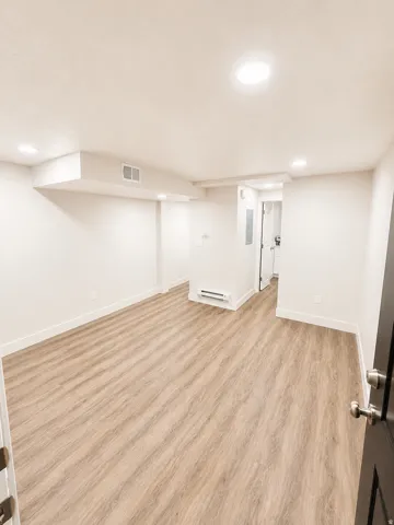 Spacious room featuring wood-finish flooring, white baseboards, and recessed lighting