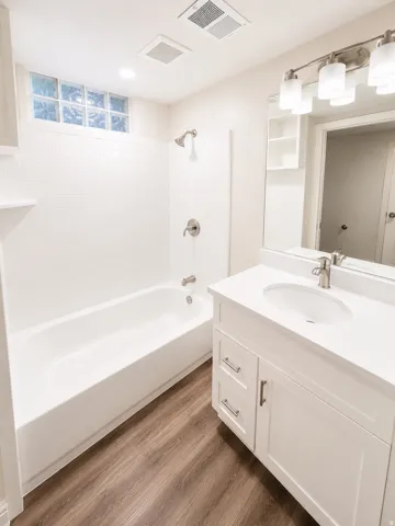 Full bathroom featuring a white vanity with an undermount sink, a white bathtub with subway tile surround, and wood-finish flooring