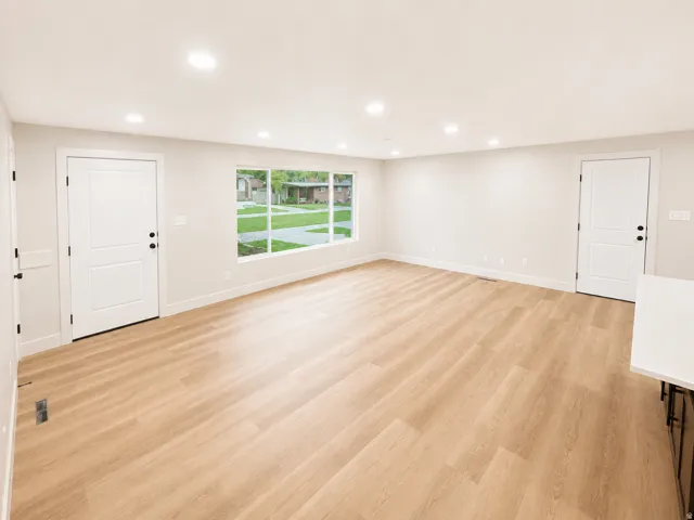 Spacious living area featuring light wood-finish flooring, recessed lighting, and a large multi-pane window