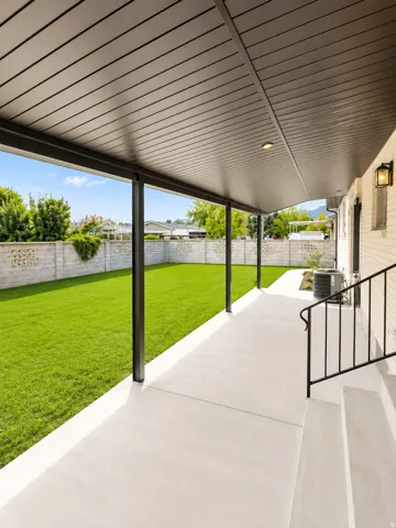 Covered patio with a smooth concrete surface, supported by black pillars, providing direct access to a manicured lawn